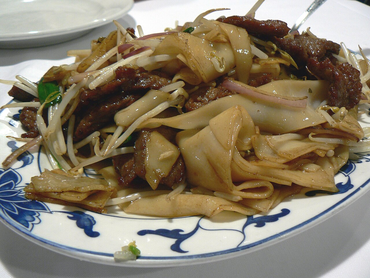 Finished Cantonese beef chow fun serving context with noodles separated, beef slices, and green onions