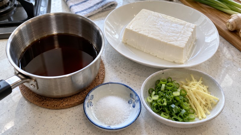 Light soy dressing prepared beside soft tofu and finely cut aromatics