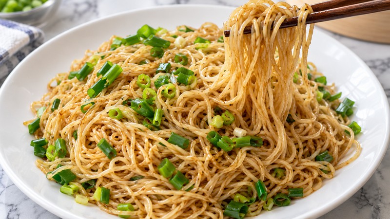 Soy-scallion tossed egg noodles lifted with chopsticks
