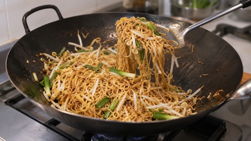 Thin Cantonese noodles and bean sprouts being stir-fried in a wok