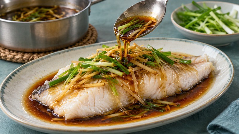 A spoon adding ginger-scallion sauce over steamed fish
