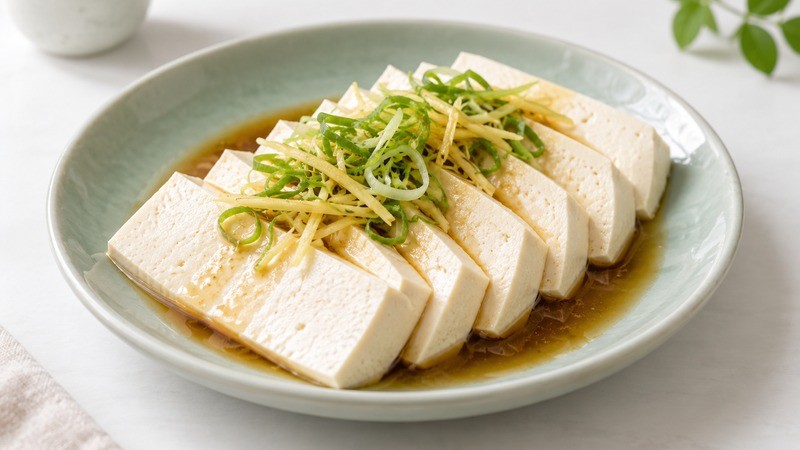 Soft tofu slices topped with ginger and scallions on a celadon plate