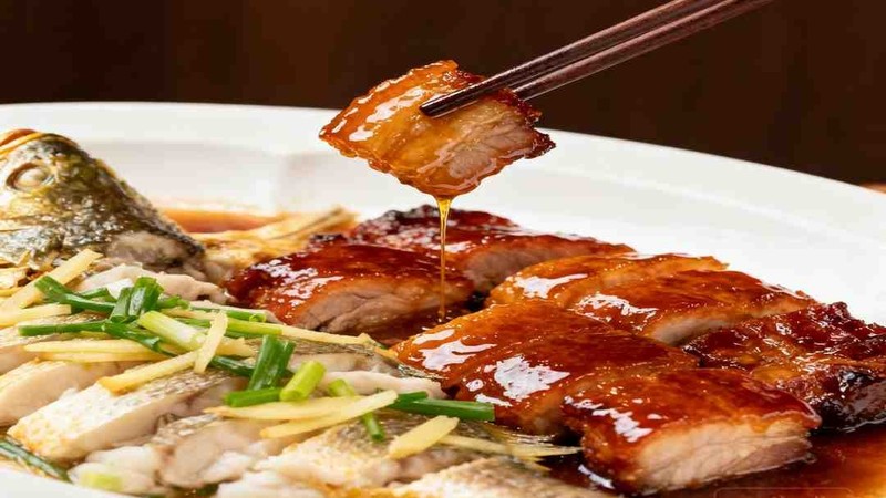 Slices of glossy cooked pork in the foreground of a meal