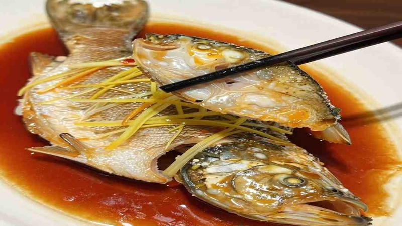 Whole cooked fish with ginger and scallion on a platter