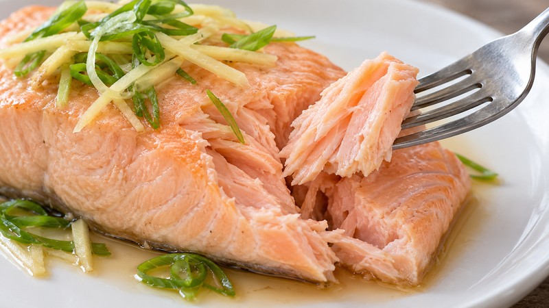 Fork separating a soft cooked salmon flake with ginger and scallion