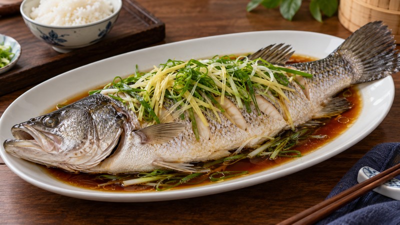 Whole steamed barramundi with ginger and scallion on a platter