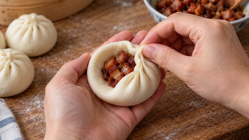 Hands pleating a dough disc around cooked pork filling