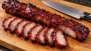 Sliced glazed pork beside a rested roast on a cutting board