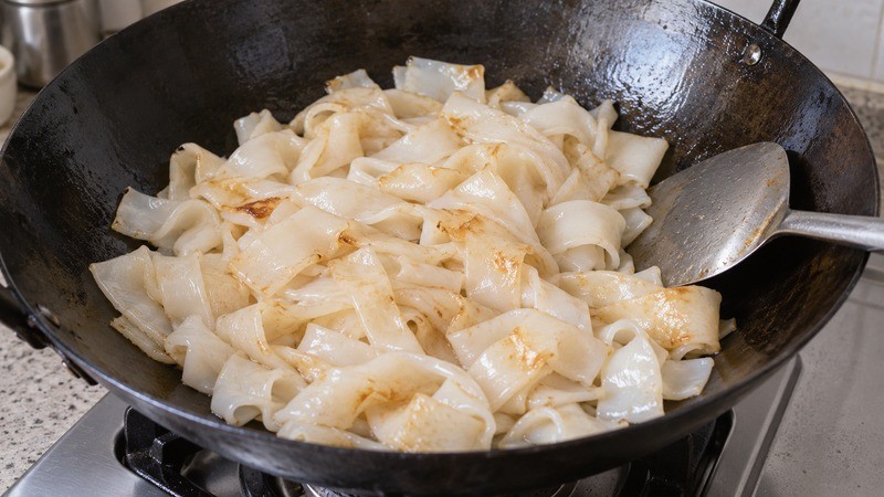 Wide rice noodles browning in a wok before sauce is added