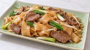 Cooked beef with broad flat rice noodles and scallions on a plate