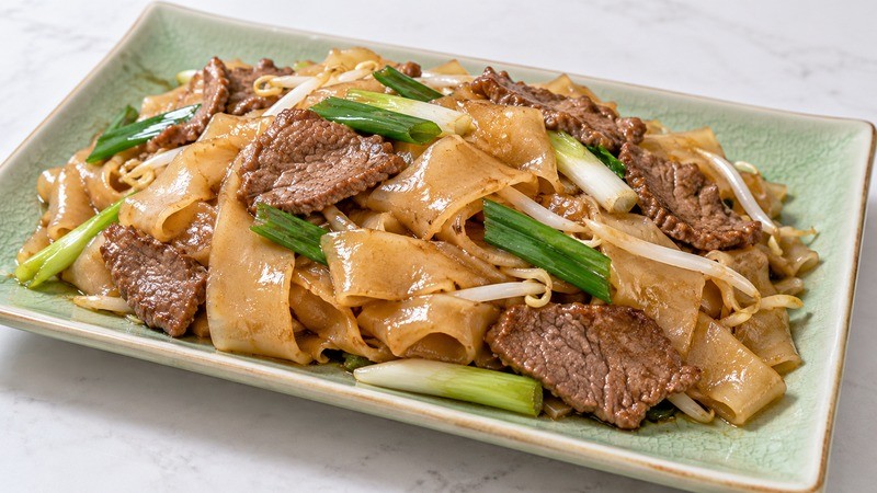 Cooked beef with broad flat rice noodles and scallions on a plate