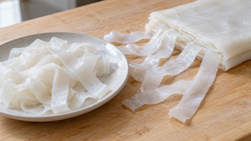 Wide rice noodle sheets being gently separated on a clean work surface