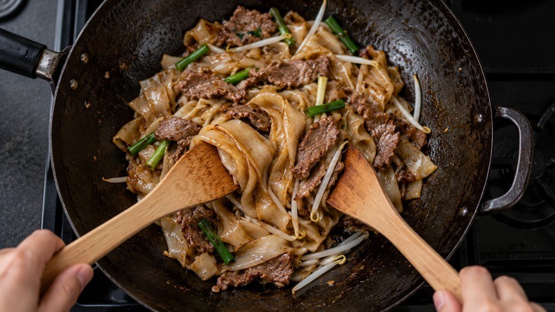 Beef slices and broad flat rice noodles being folded in a wok
