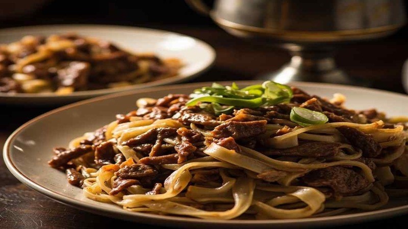 Beef over broad flat noodle ribbons on a plate