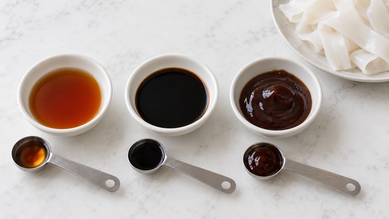 Three small bowls of light soy sauce, dark soy sauce and oyster sauce with measuring spoons