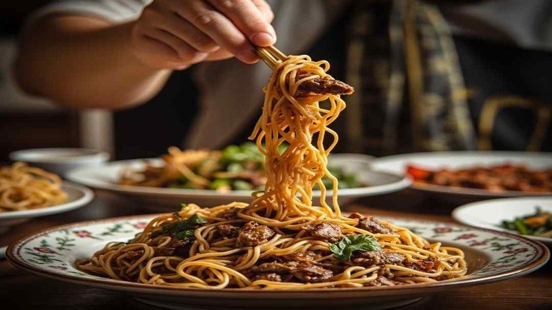 Chopsticks lifting yellow noodles and beef from a platter