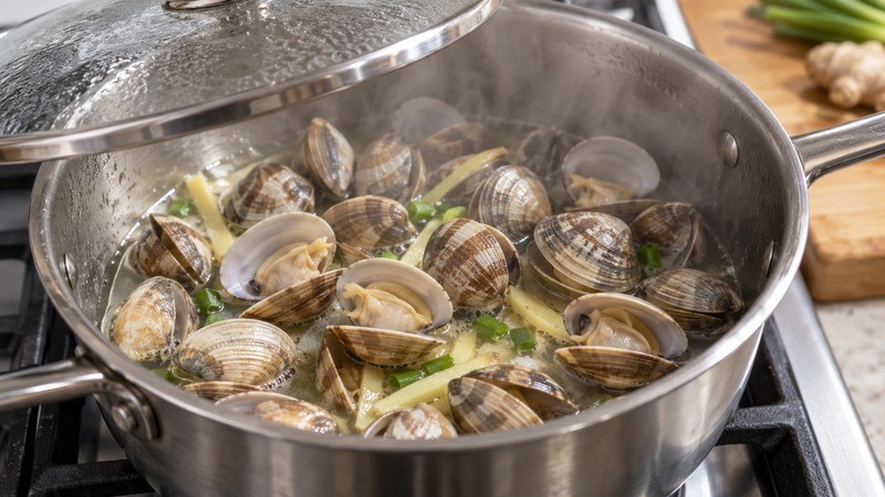 Clams opening in a lidded saucepan with a small amount of ginger-scallion cooking liquid