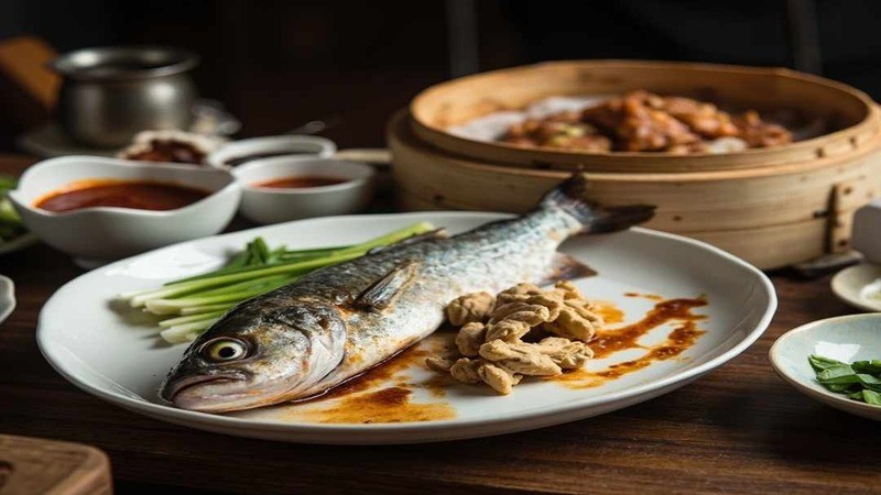A whole fish beside ginger pieces on a white platter