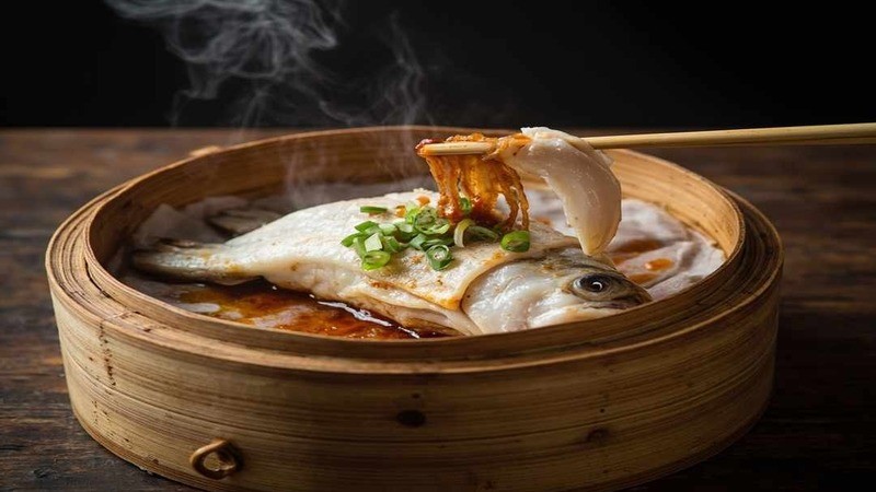 Chopsticks lifting fish flesh from a fish in a bamboo vessel