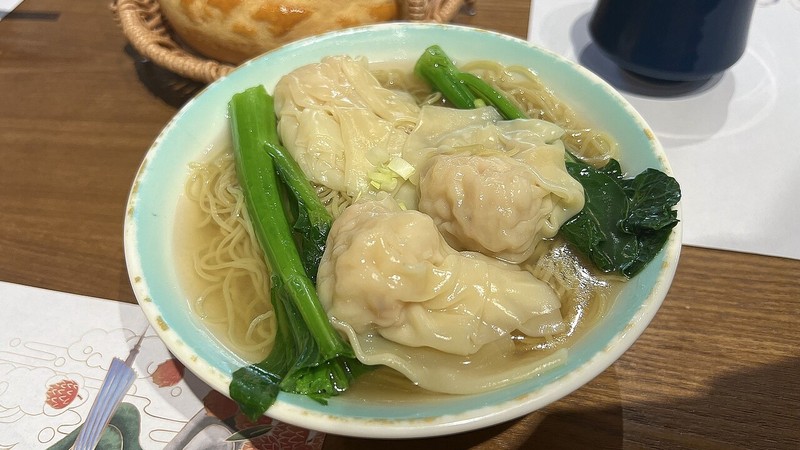 Served wonton soup with greens in a white bowl