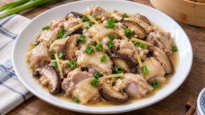 Finished Cantonese steamed chicken with sliced shiitake and ginger in a shallow rimmed plate