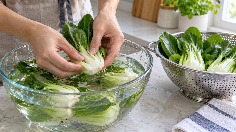 Bok choy stem bases being cleaned in a bowl of water beside a colander