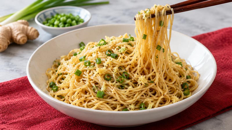 Lightly coated ginger scallion noodles with strands lifted by chopsticks