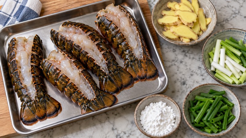 Prepared lobster tails beside sliced ginger and separated scallion whites and greens