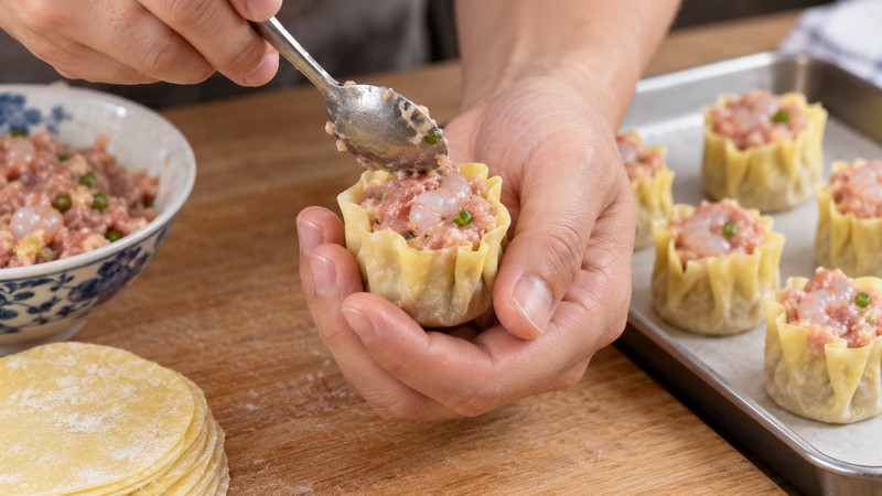 Hands shaping an open-top siu mai with a flat base