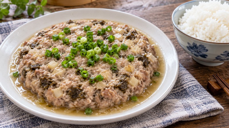 Steamed pork patty with scallions and cooking juices beside rice
