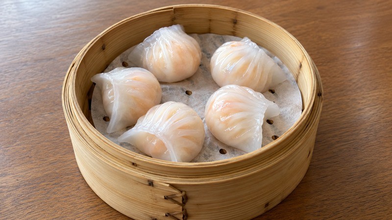 Five translucent har gow shrimp dumplings in a bamboo steamer