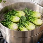 Halved baby bok choy arranged in a single layer in a stainless-steel steamer basket