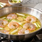 Shrimp gently poaching in butter with ginger and scallion in a shallow skillet